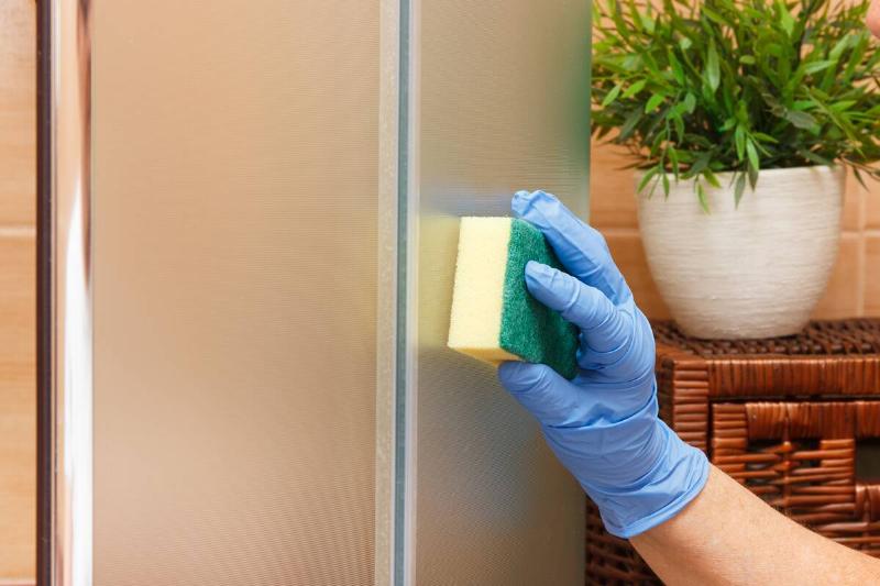 Hand washing a stainless steel fridge with a sponge. 