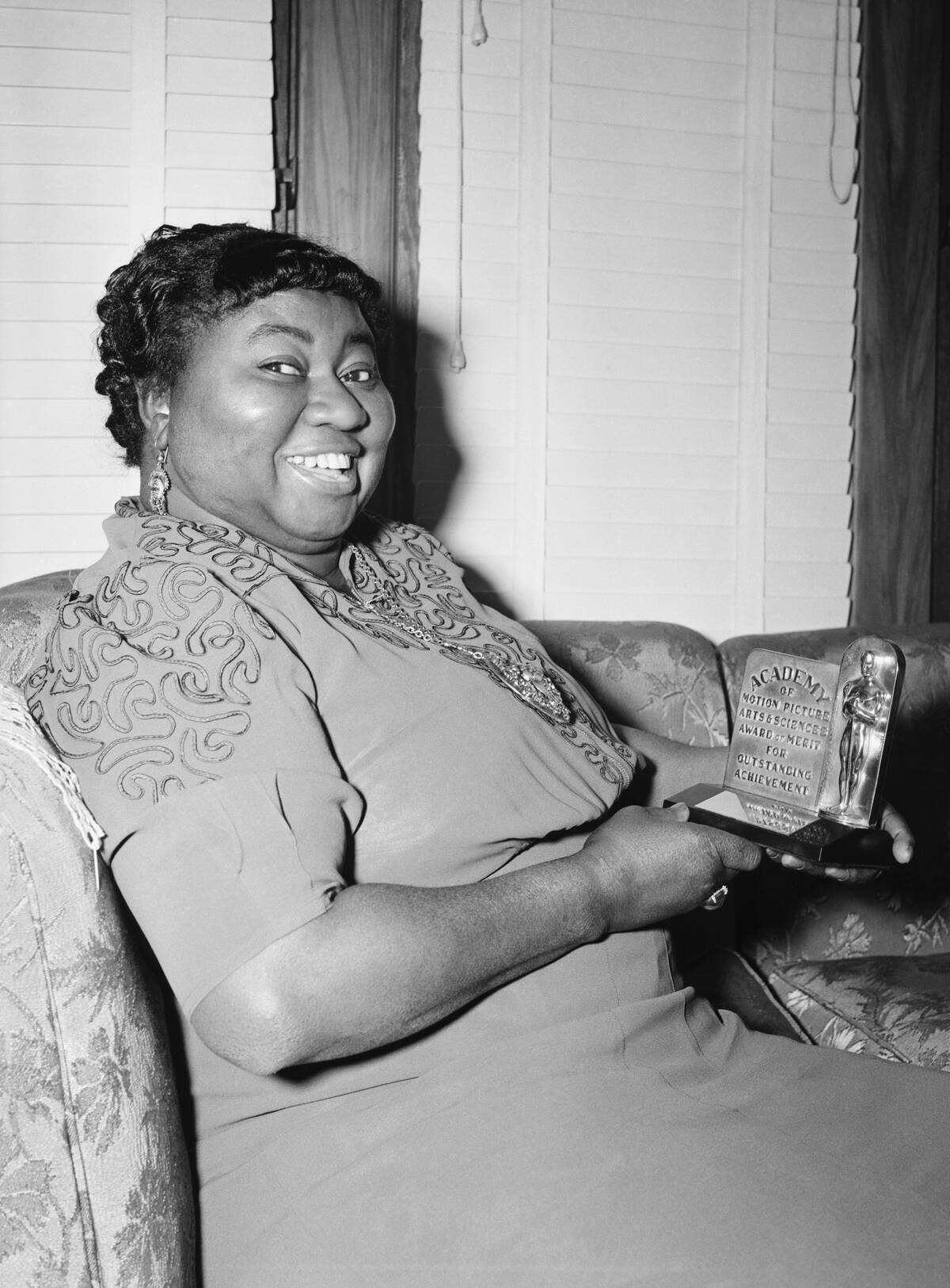 Hattie McDaniel sitting on a couch while holding her Academy Award