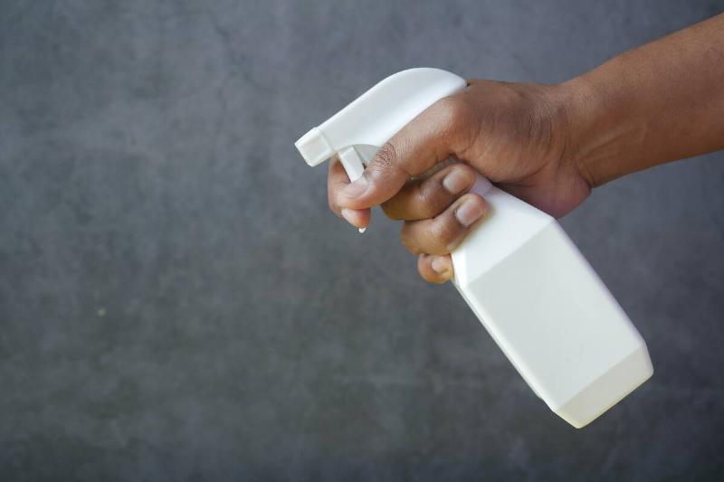 Person holding a white spray bottle in front of grey background. 