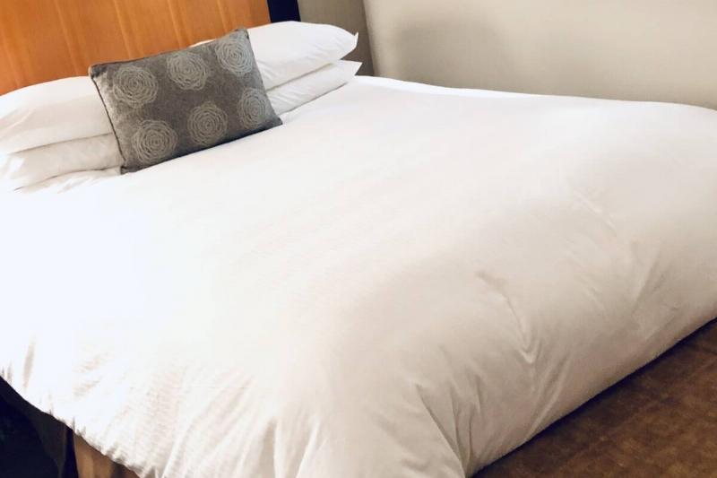 Кровать-номер-отеля-с-белым-покрывалом-2026-01-06-09-13-41-utc Гостиничный номер с белым одеялом на кровати.