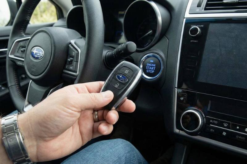 A hand holding a key fob up to the start button of a car. 