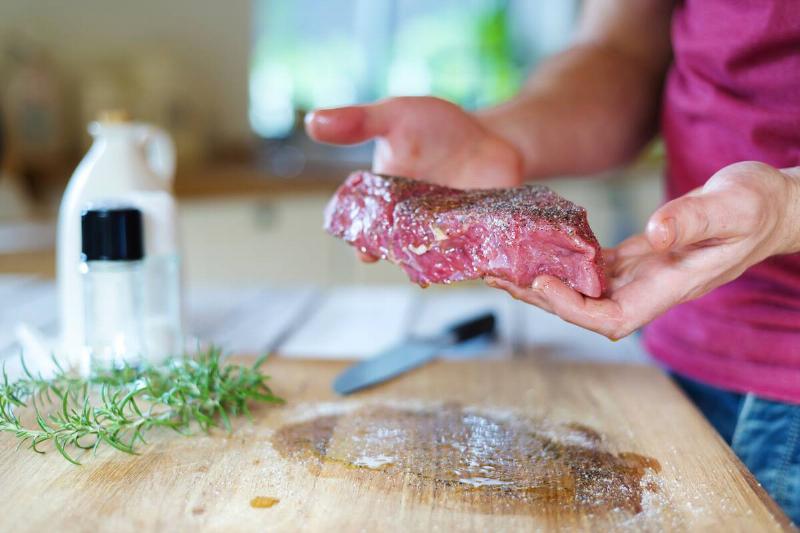 Man holding raw meat in the kitchen. 