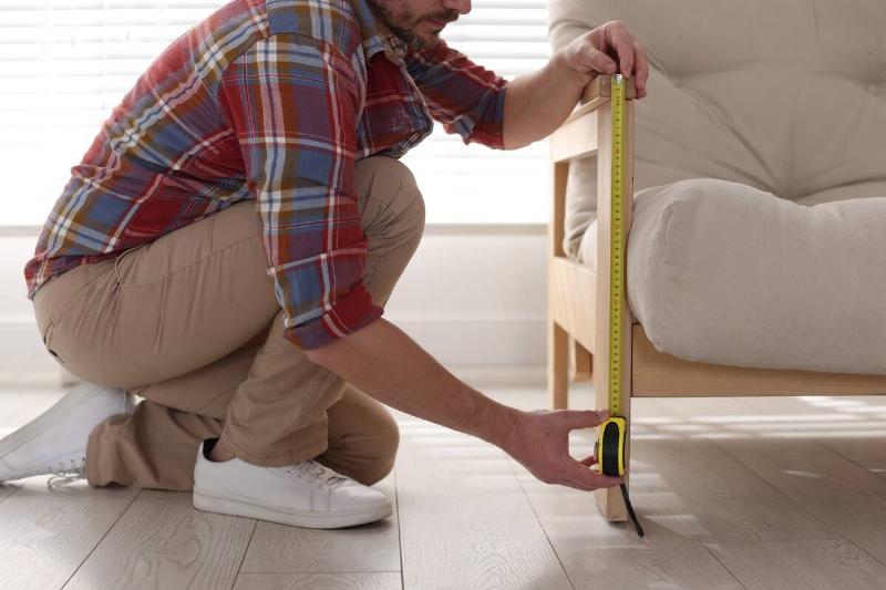 Man measuring height of gap under couch. 