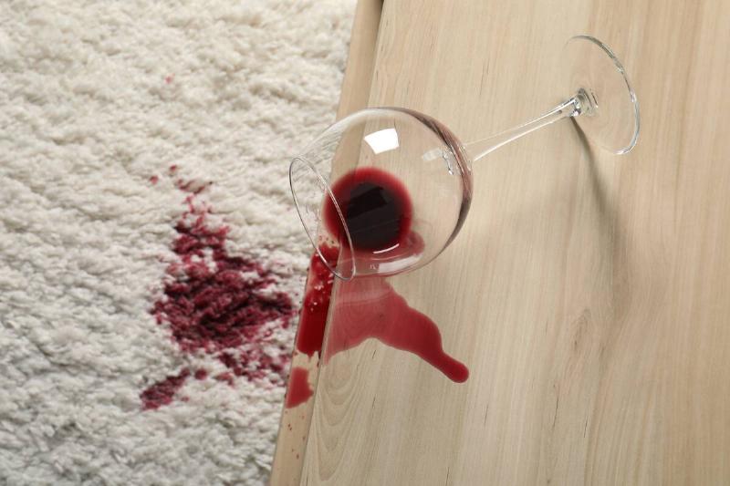 Overturned glass and spilled red wine on white carpet indoors.