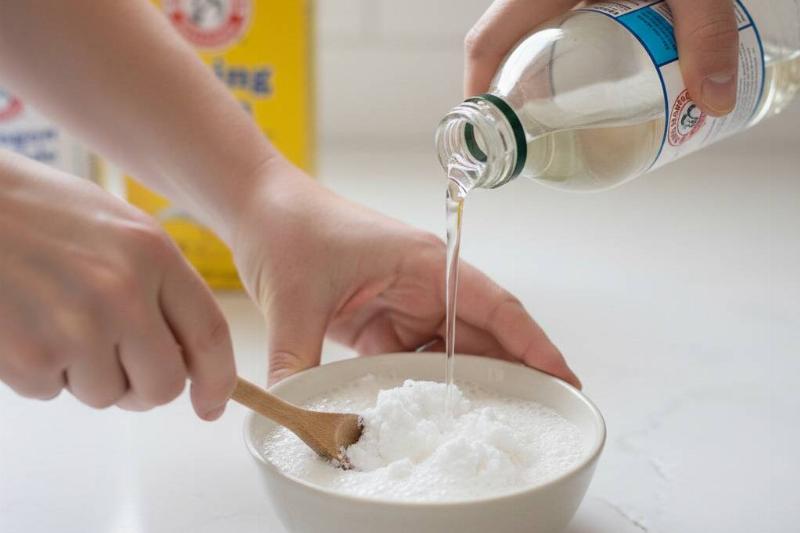 Hands making a paste out of vinegar and baking soda.