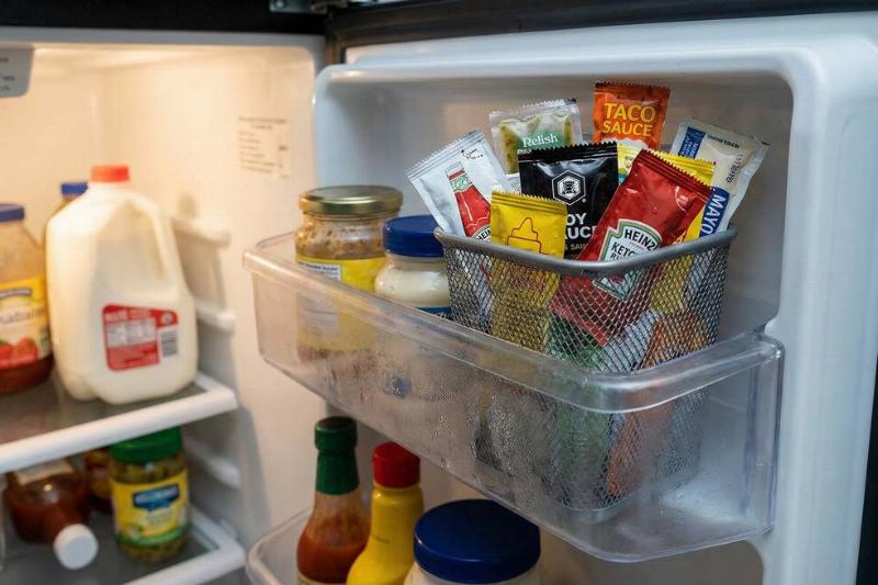 A pencil holder being used to hold condiment packets in a fridge. 