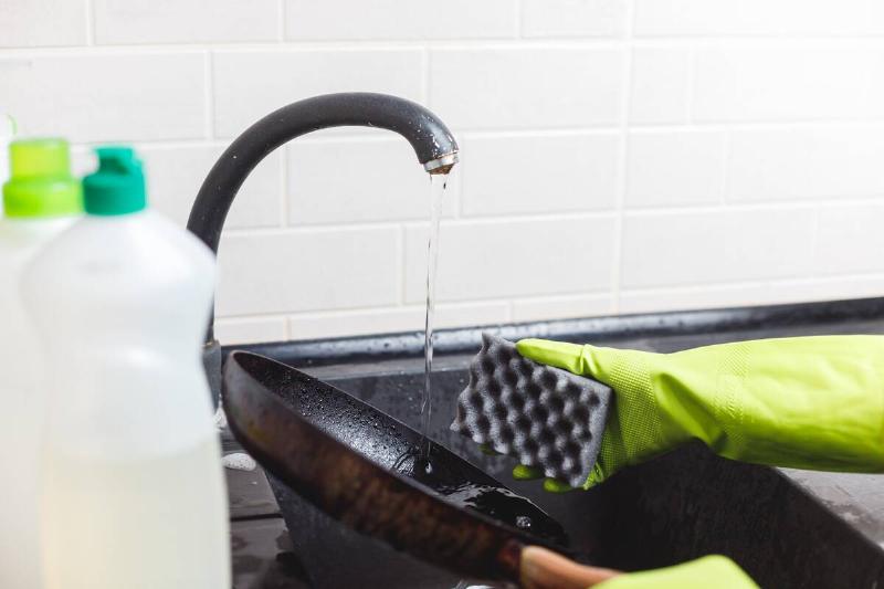 Person washing a non-stick frying pan with a sponge. 