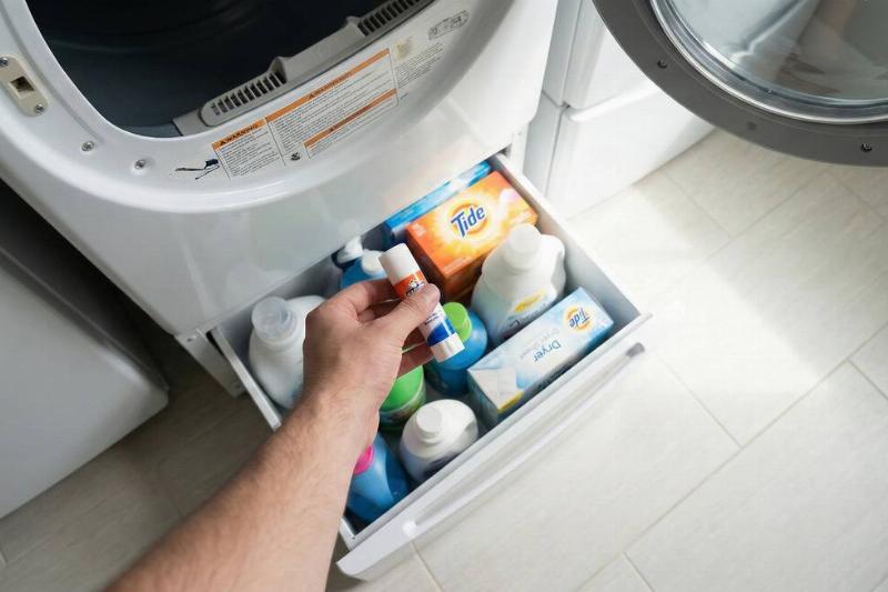 A hand putting a stain remover stick in a pedestal under a dryer. 