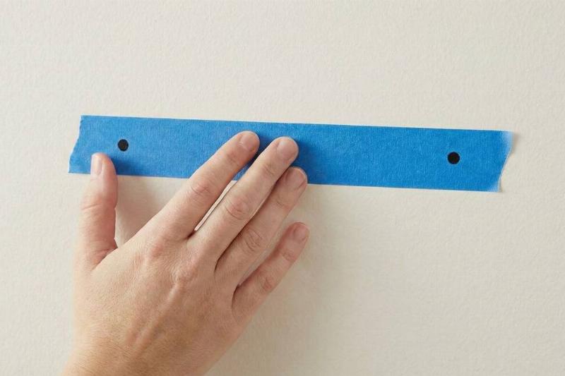 A hand holding the tape with the frame marks on the wall. 