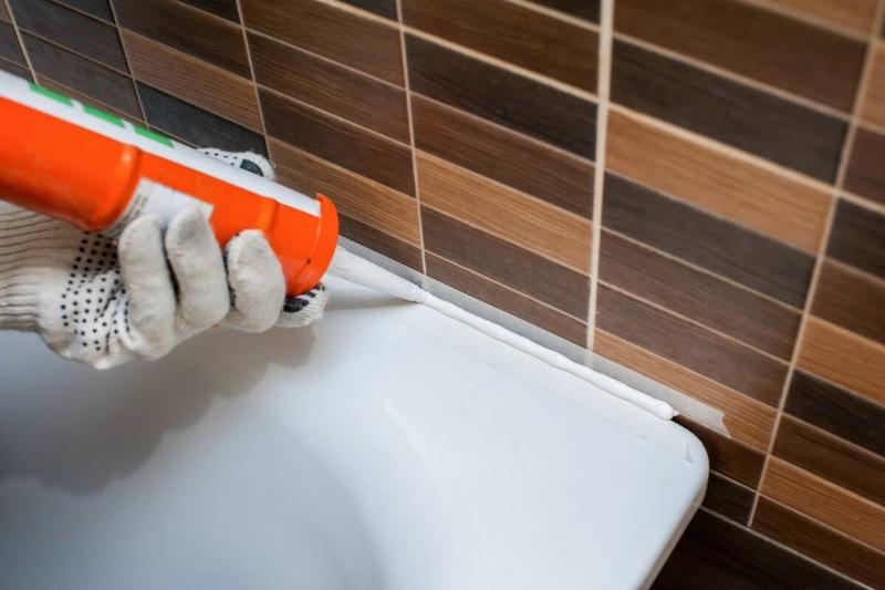 A person sealing the crack around a bathtub with silicone sealant. 