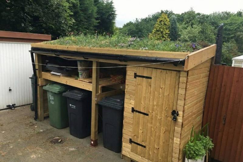 выбрасывать мусор Сарай с крышей из ящика для цветов и мусорными баками внутри.