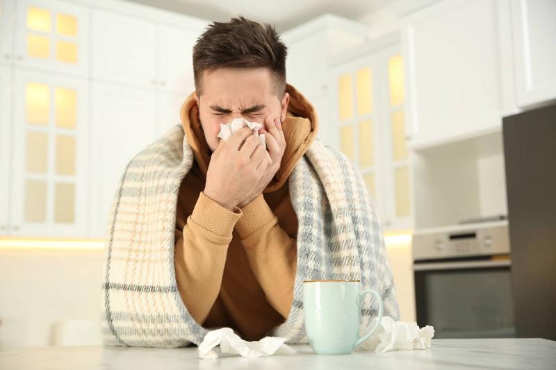 Man blowing his nose with mug of tea.