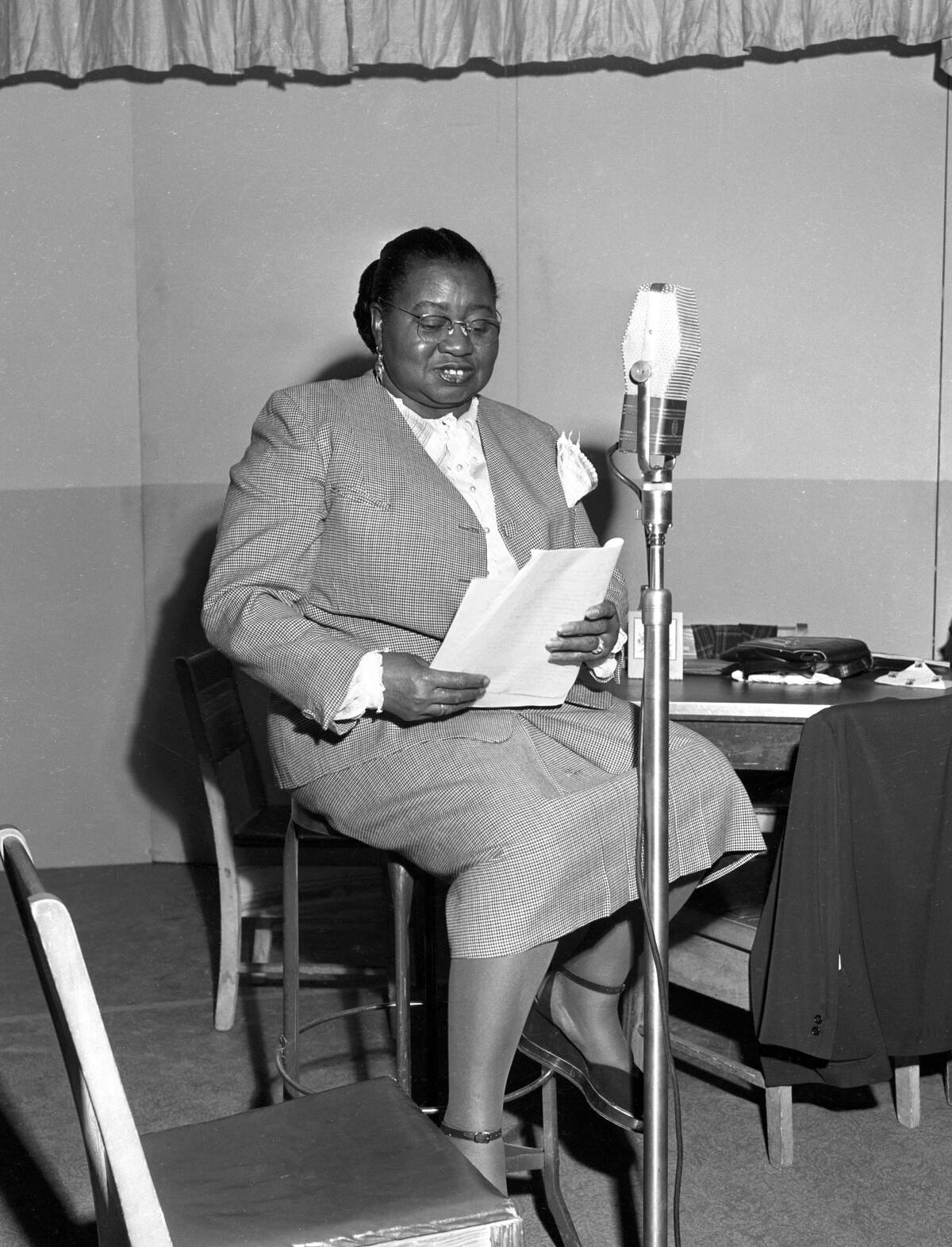 Hattie McDaniel sitting at a microphone, looking down at a script