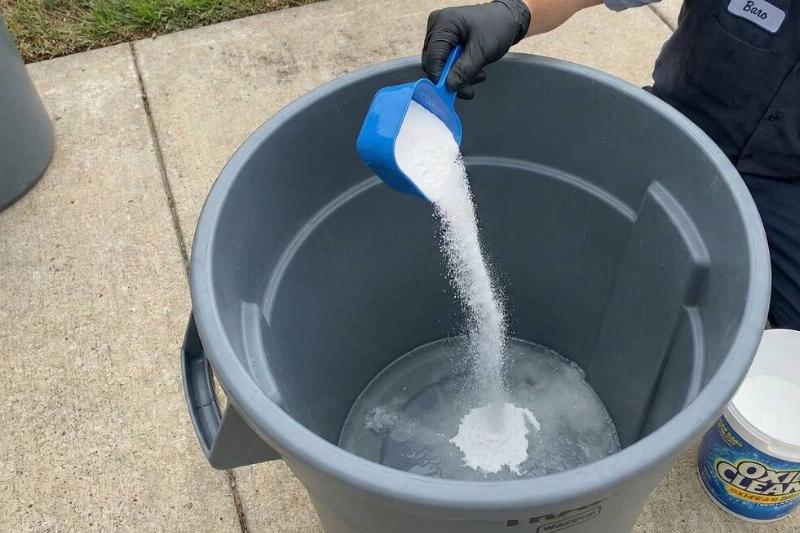 мусор Человек кладет ложку OxiClean на дно мусорного бака.