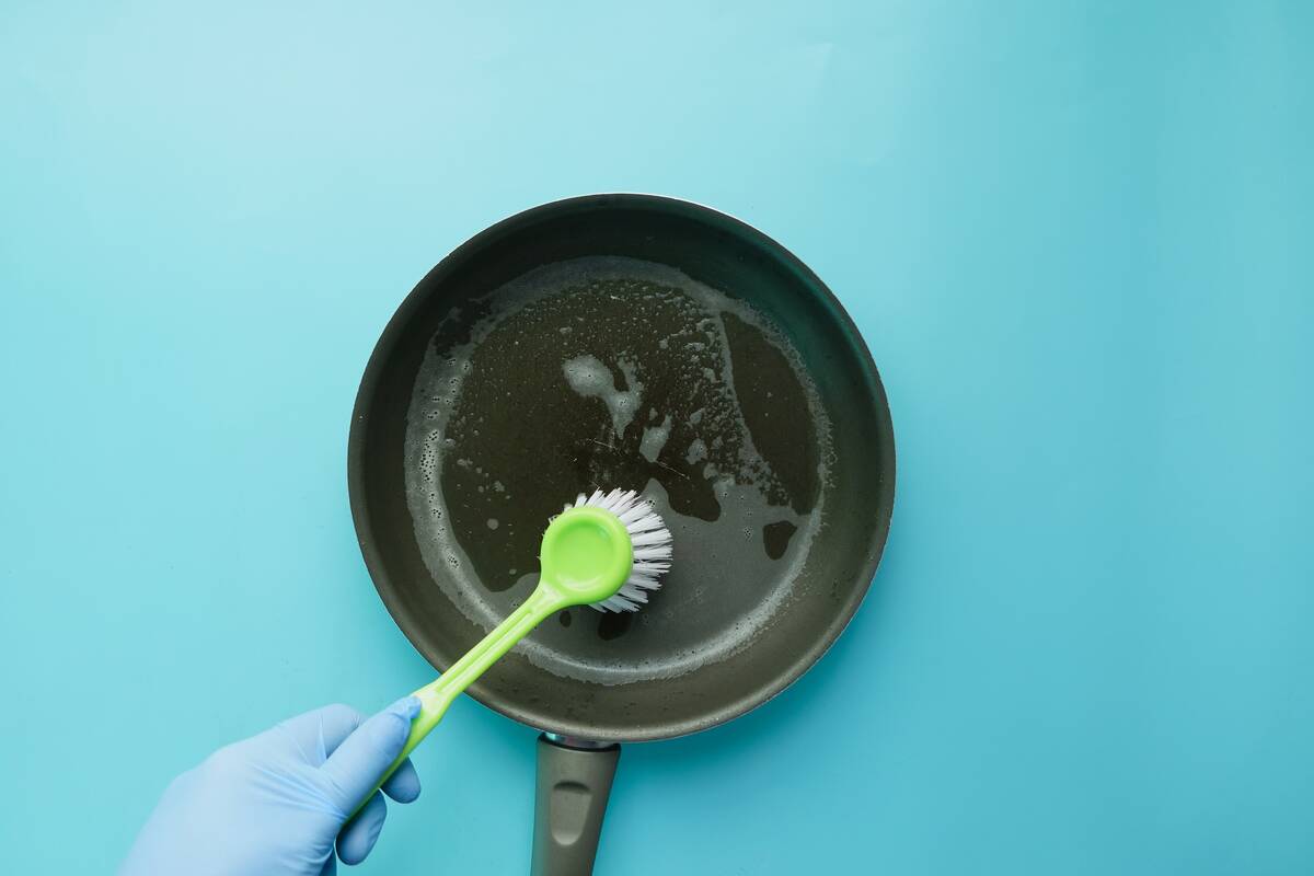 A person scrubbing a cast iron pan with a brush. 