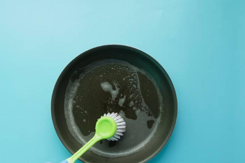 мытье-кухонные принадлежности-щеткой-2026-01-06-10-21-14-utc Человек чистит чугунную сковороду щеткой.