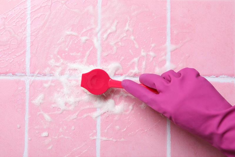 Person cleaning pink tiles with brush.