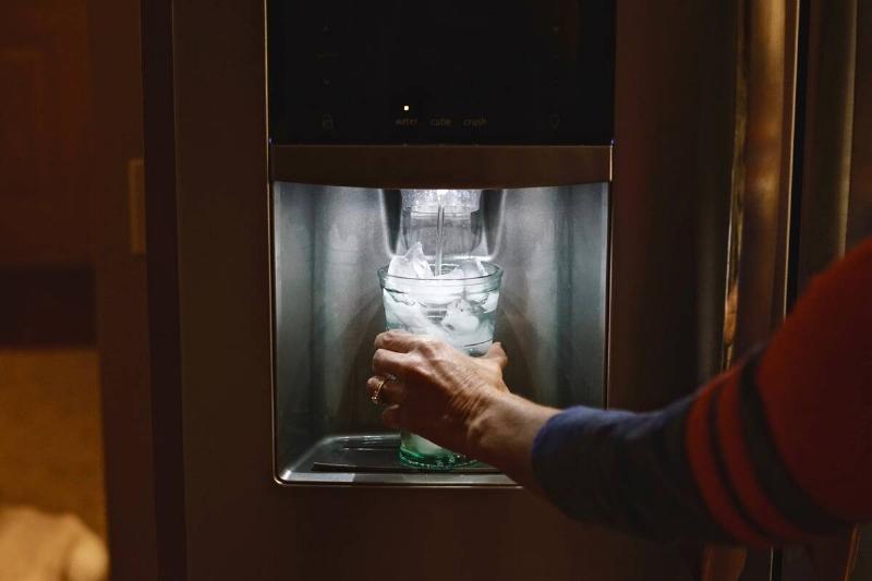 A person filling a glass of water from a fridge water filter. 