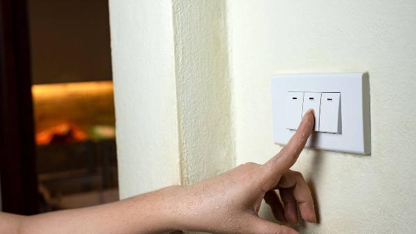 Hand pressing light switch to turn off lights. 