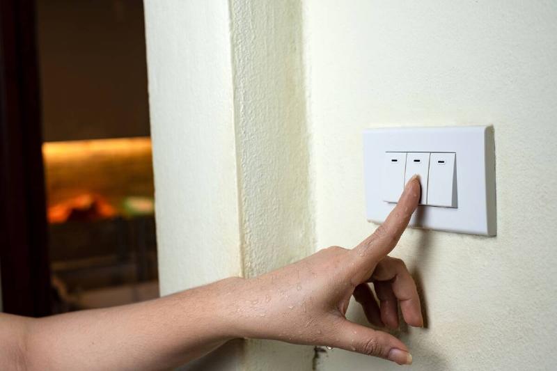 Hand pressing light switch to turn off lights. 