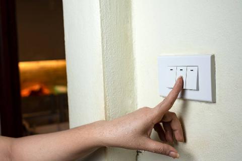 Hand pressing light switch to turn off lights. 