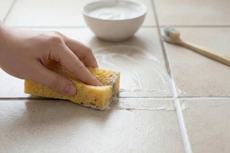 A sponge wiping away the leftover paste on grout.