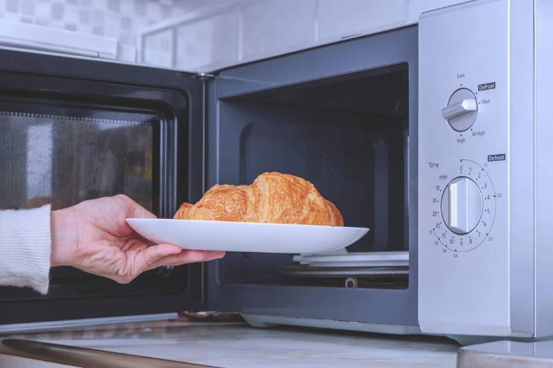 Hand putting food into a microwave. 