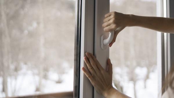 A  woman is seen opening a window in her home.