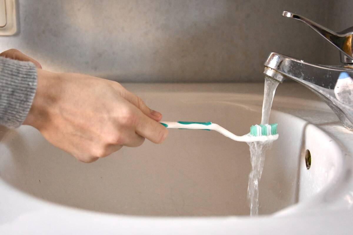 A person rinsing their toothbrush under water at the sink.