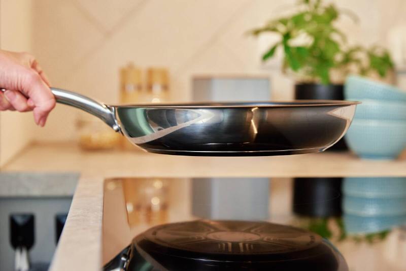 A person holding a steel frying pan over a stove. 