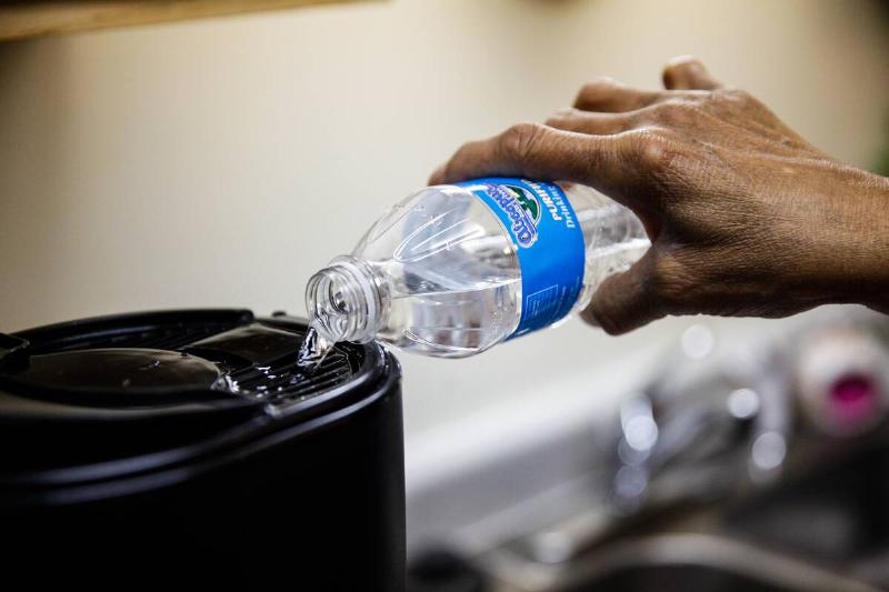 Person pouring bottled water into coffee machine. 