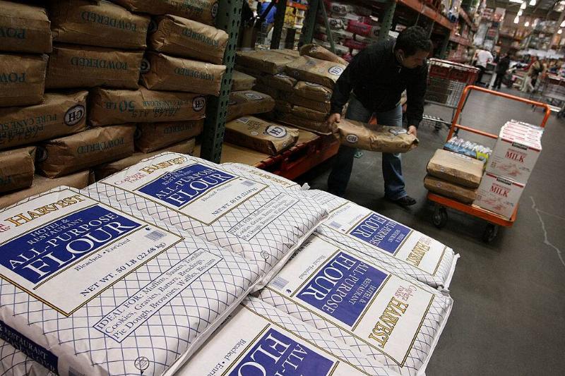 Man lifting a large bag of rice into a cart, near piles of flour