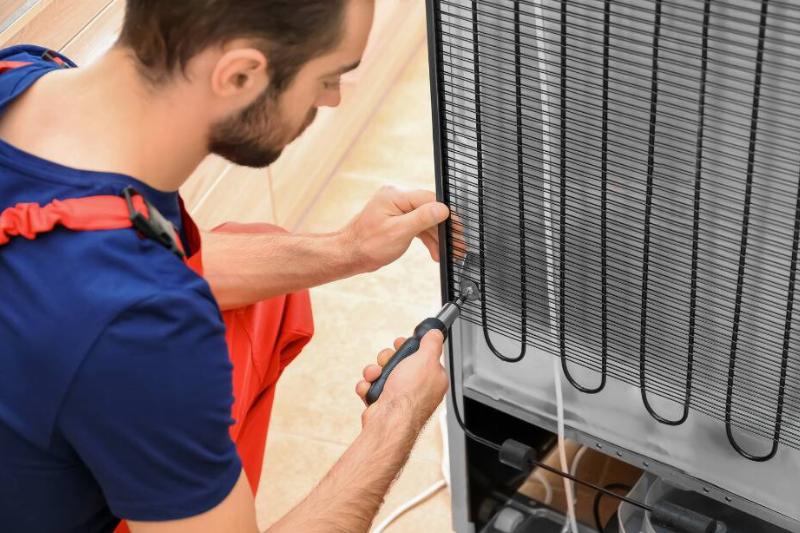 Technician repairing the coils on the back of a fridge. 