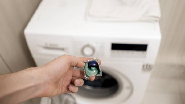 Hand holding laundry pod in front of washing machine. 