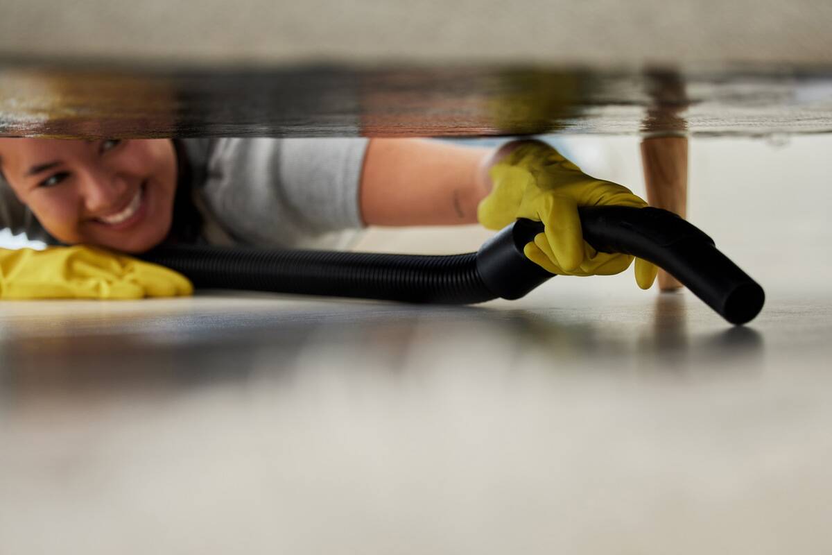 Woman using long, flexible vacuum attachment to clean under couch. 