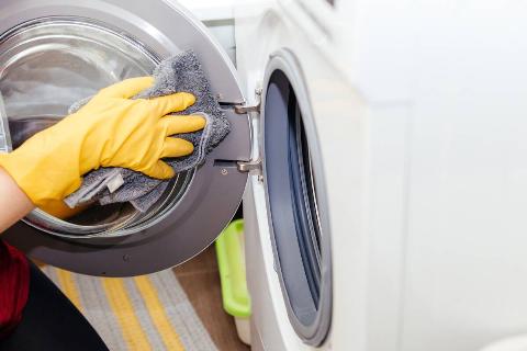 Hand in yellow gloves wiping seal of washing machine door with cloth. 