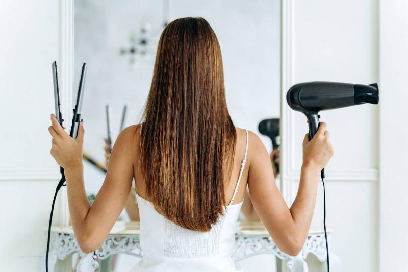 A woman holding a hair dryer and hair straightener. 