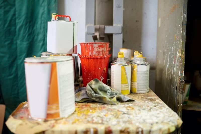 Old paint cans and containers of paint thinner on a table. 