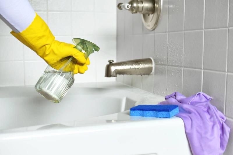 A gloved hand washing a bathtub. 