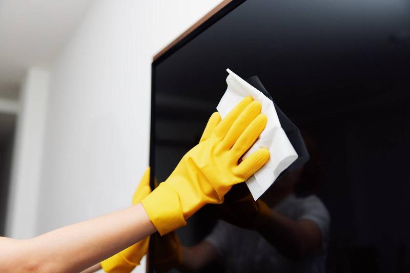 Hand in yellow glove wiping a flat screen TV with paper towel. 