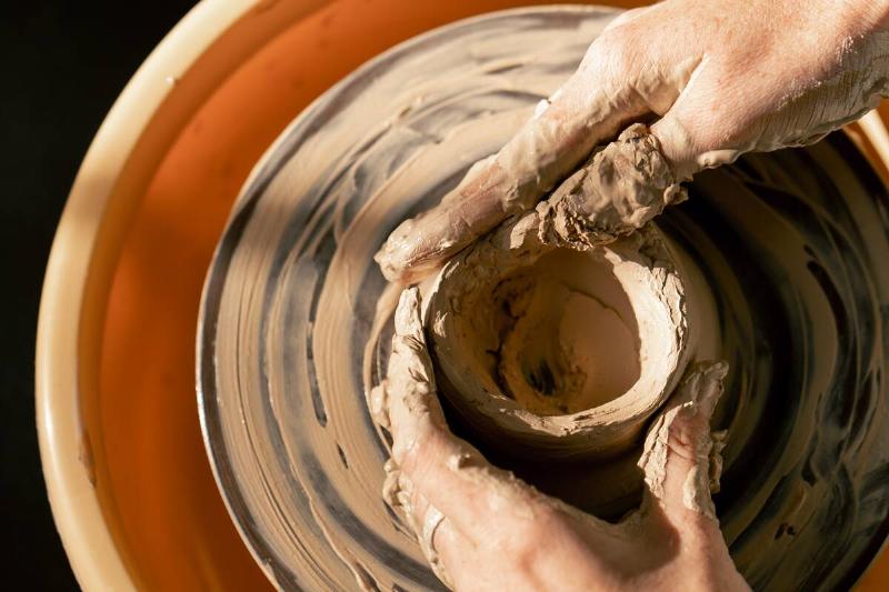 Person off-screen molding clay on a potter's wheel