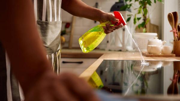 Man spraying cleaner on glass-top stove. 