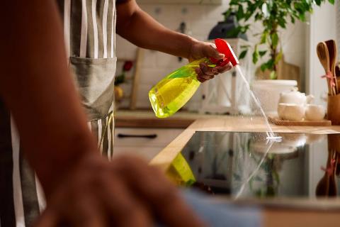 Man spraying cleaner on glass-top stove. 