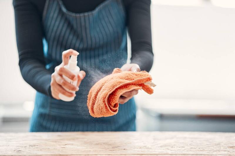 A person spraying cleaning spray on a microfiber cloth. 