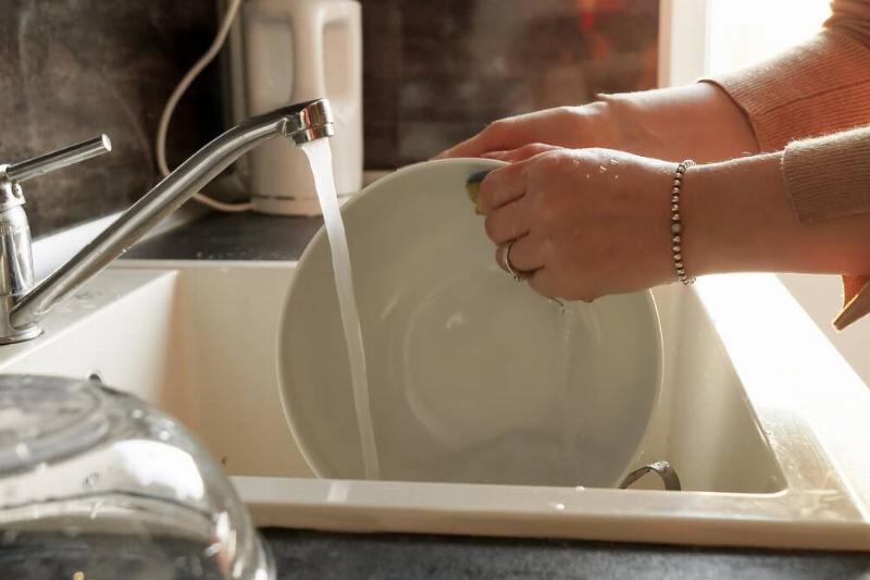 Closeup of woman washing dishes in sink with sponge.