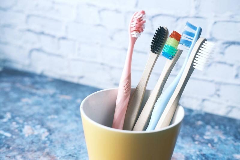 Colorful toothbrushes in white mug on a counter. 