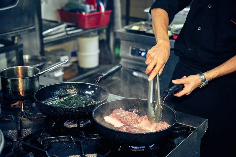 Person off-screen cooking meat in a frying pan