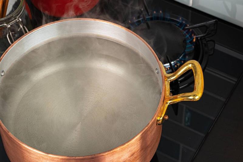 Copper pot with boiling water on a gas stove.