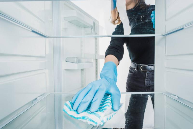 Hand in gloves cleaning fridge shelf. 