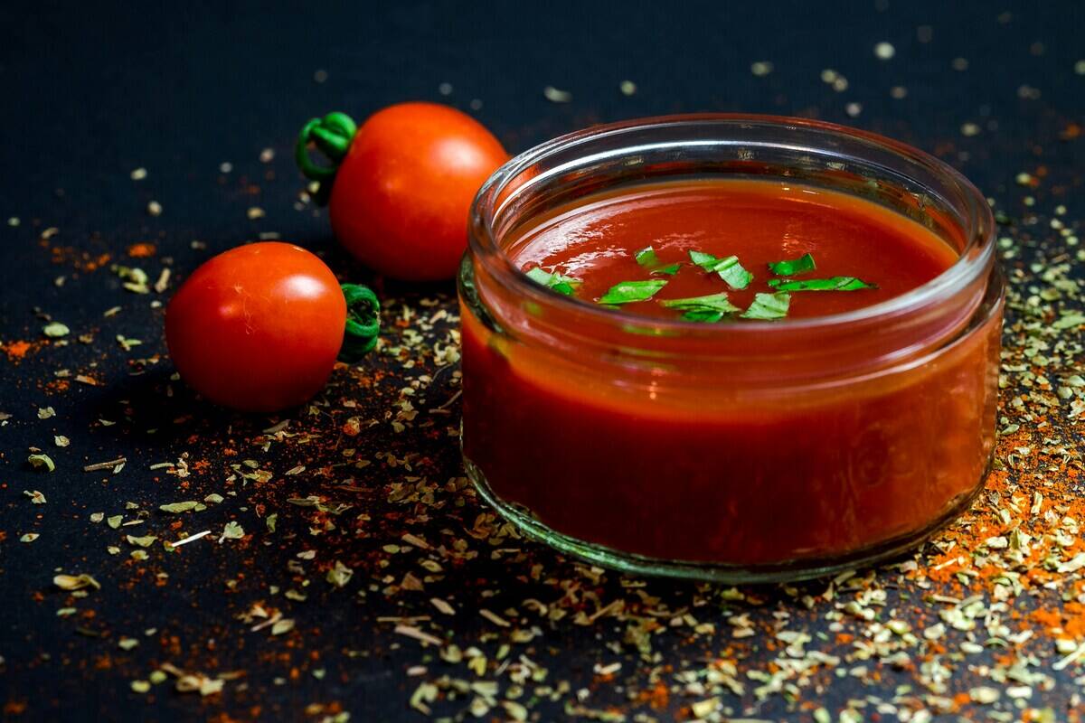 Tomato paste in a glass bowl. Two cherry tomatoes and random flecks are on the surface around the bowl